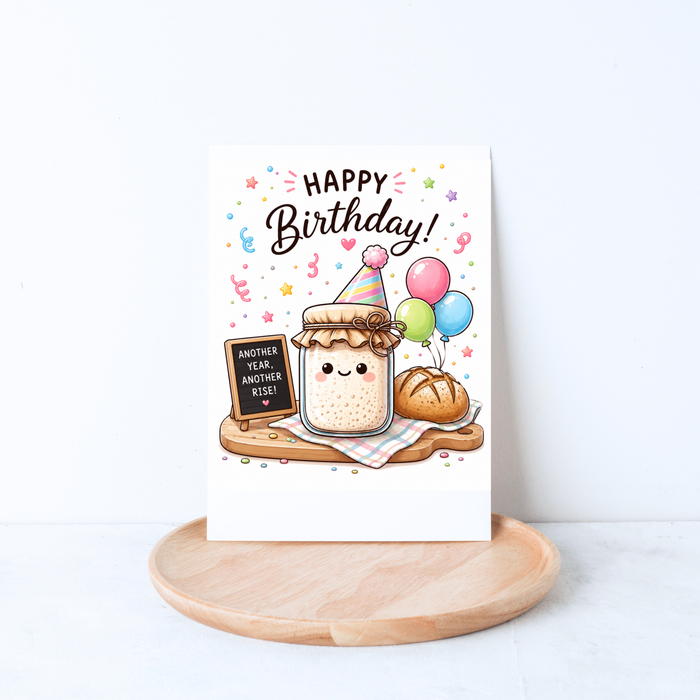 Whimsical sourdough birthday greeting card displayed in a cozy lifestyle mockup with a kraft envelope, flowers, and a coffee mug.