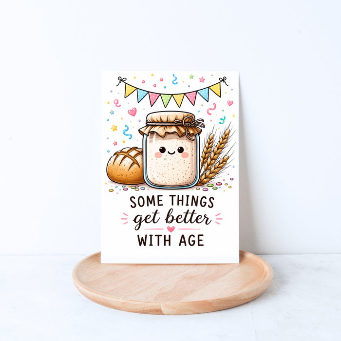 Cute bread-themed birthday card with sourdough starter, wheat stalks, and colorful bunting in a lifestyle mockup.