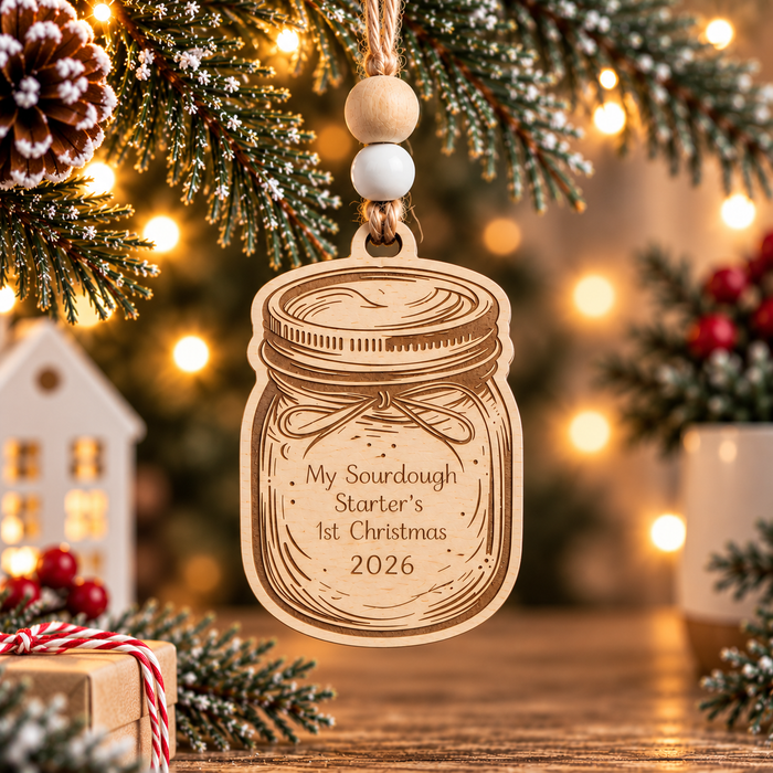 Light wood sourdough starter Christmas ornament shaped like a mason jar, laser engraved with My Sourdough Starter's 1st Christmas 2026, hanging from a festive evergreen branch.