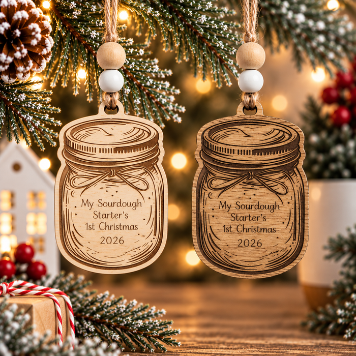 Light and dark wood sourdough starter Christmas ornaments shaped like mason jars, laser engraved with My Sourdough Starter's 1st Christmas 2026, displayed together on festive evergreen branches.